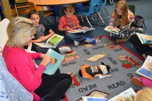 Teacher sitting on rug with several students. Each person is holding a copy of the book Buddy Unchained, a book about a dog, and smiling.