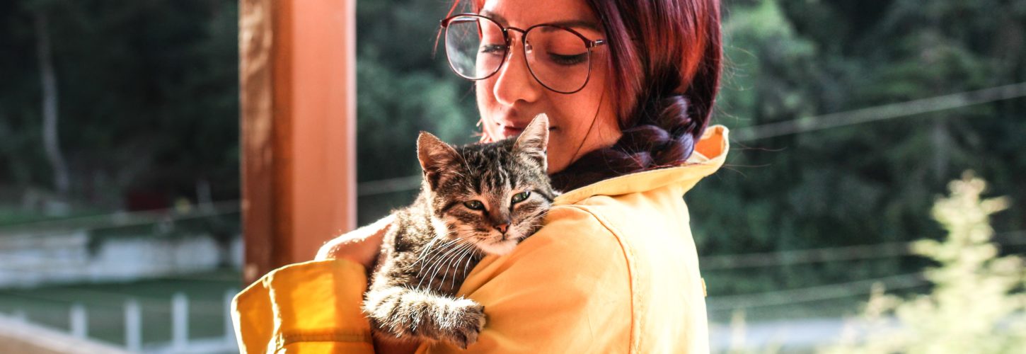 Woman holding cat on her shoulder, looking down at her lovingly on a porch