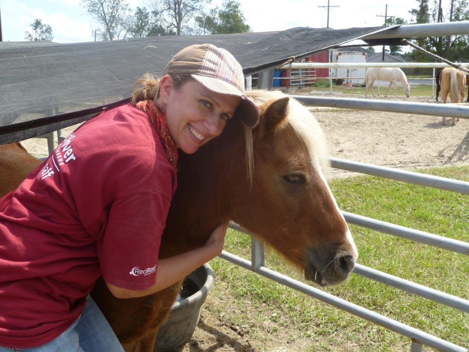 A woman in a RedRover Responders tshirt wearing a tan hat hugs a brown pony