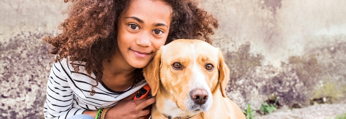 Beautiful african american girl with curly hair outdoors with her cute dog against old concrete wall.