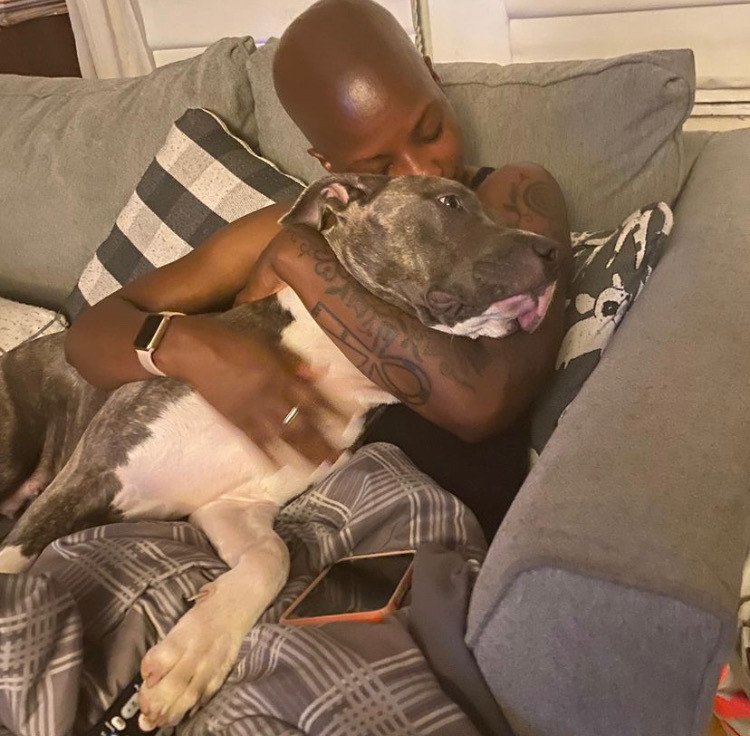 Dr. Duncan sits on a gray couch hugging her gray and white pitbull who is lying across her lap.