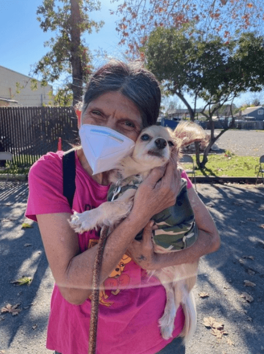 A woman holding her small dog looking at the camera