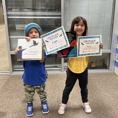 Two young children holding books and certificates