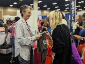 woman wearing a beige jacket handing out a t-shirt