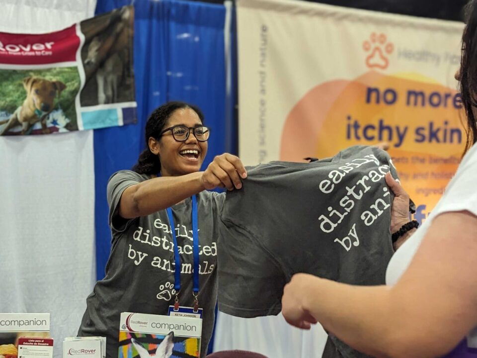 woman wearing glasses handing out t-shirt with the caption "Easily distracted by animals"