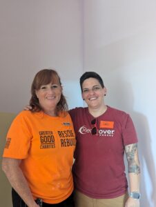 Two women, one with red hair and an orange Rescue Rebuild shirt, one with short brown hair, sunglasses, and a red RedRover Responders shirt