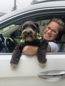 woman in car at drive-through wellness clinic holds curly black dog up