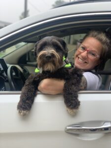 woman in car at drive-through wellness clinic holds curly black dog up