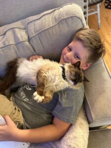 Child holds Himalayan cat from The Pretty Pittie Committee February 2025 deployment on the couch