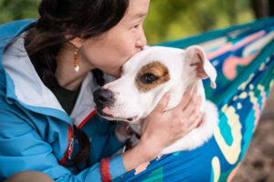 woman wearing a pearl earring kisses her terrier mix dog on the forehead wrapped in a blanket