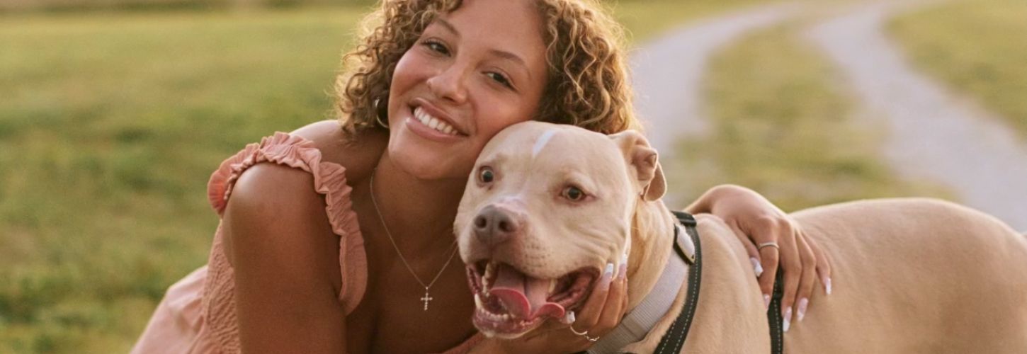 woman kneeling down smiling and hugging her Pitbull