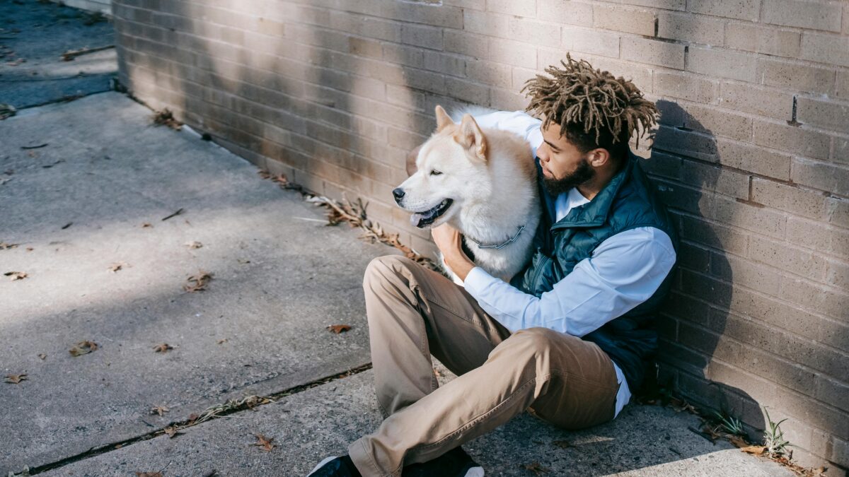 man sits on the ground hugging his large white dog
