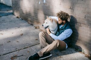 man sits on the ground hugging his large white dog