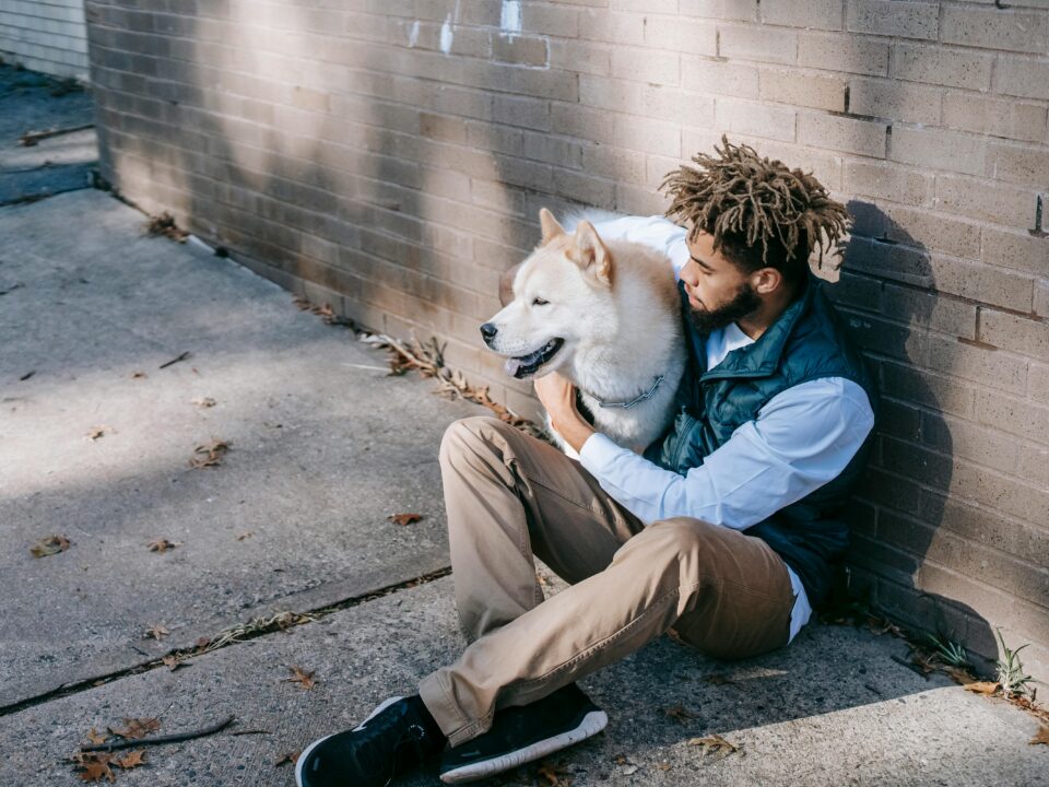 man sits on the ground hugging his large white dog
