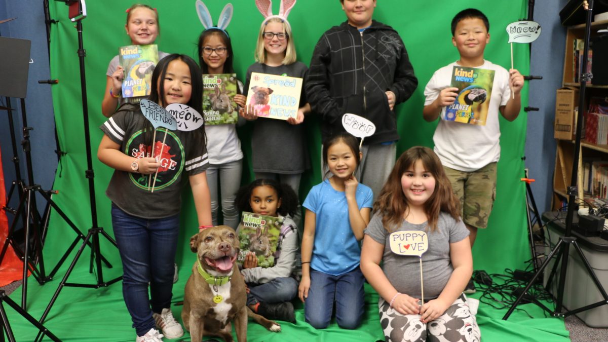 A classroom poses with Kind News magazine and a dog